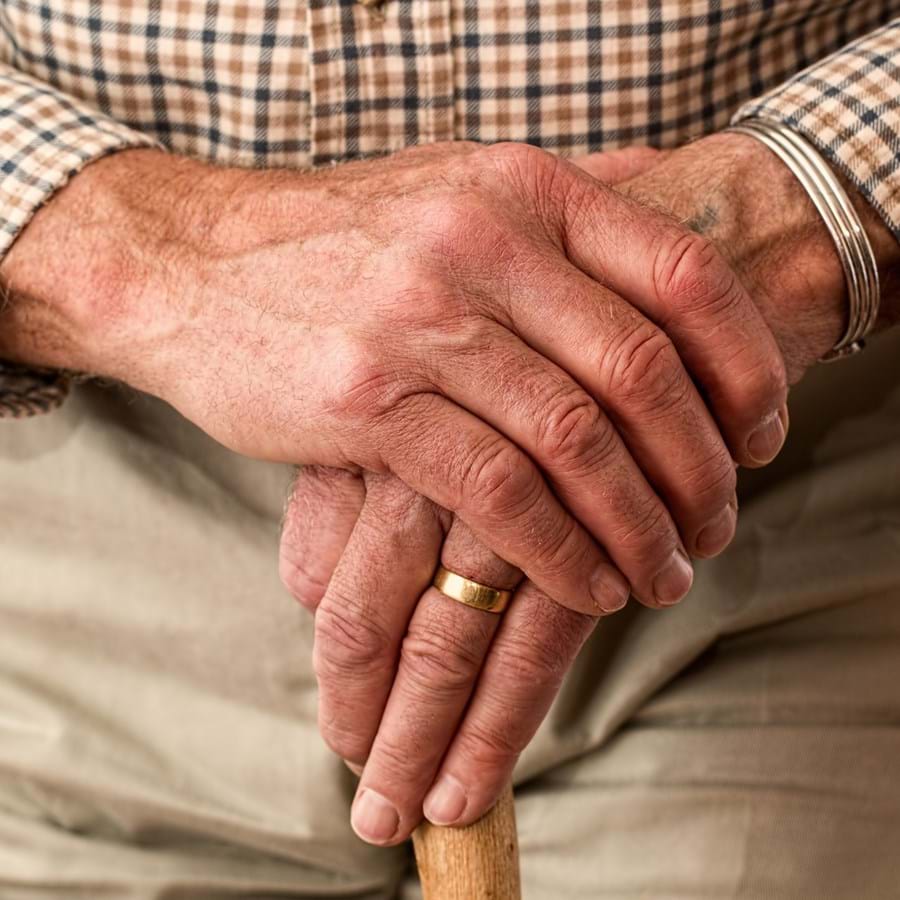 Senior legt beide Hände auf Griff des Gehstocks