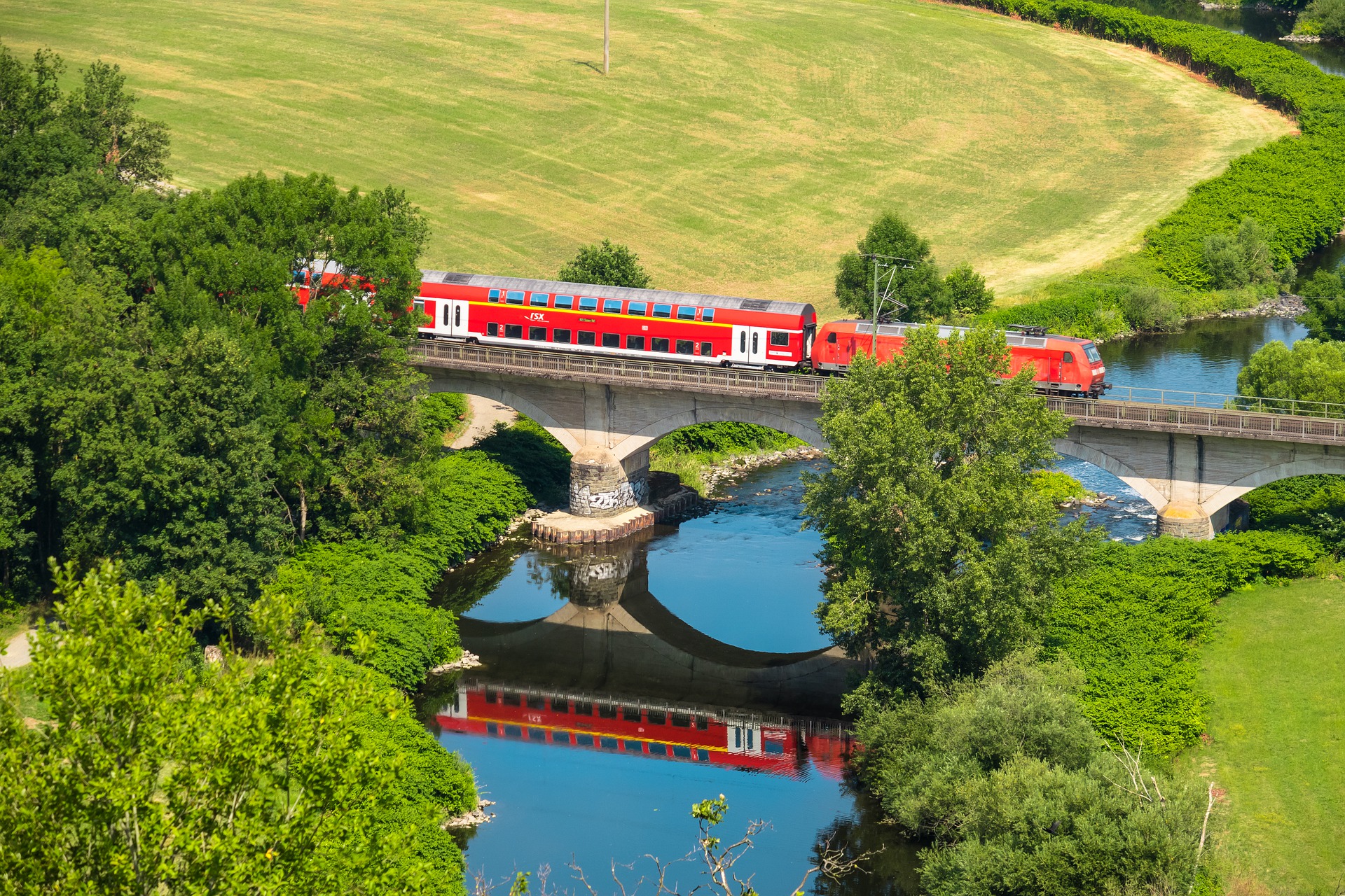 Zug fährt in idyllischer Gegend auf Bahnbrücke über einen Fluss