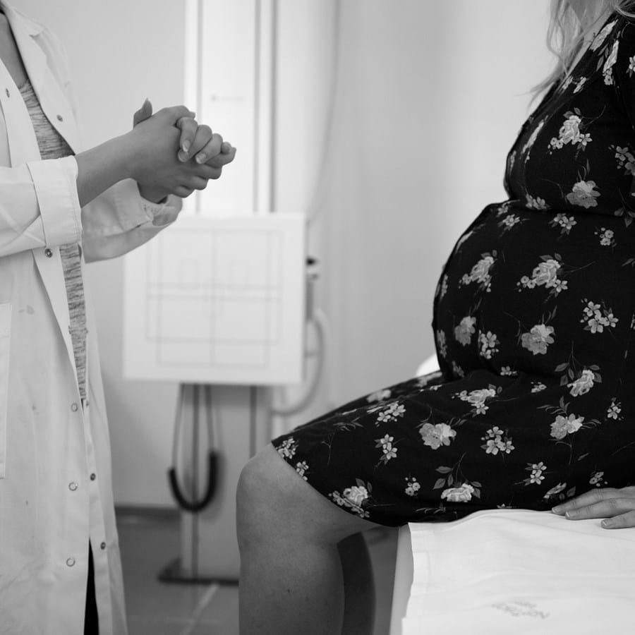 Frauenärztin berät eine schwangere Frau, welche auf einer Liege sitzt