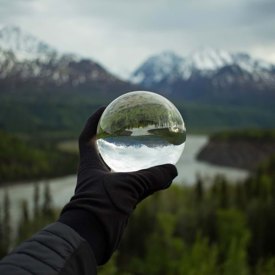 eine Person hält Glaskugel in die Landschaft aus Bergen und Wäldern