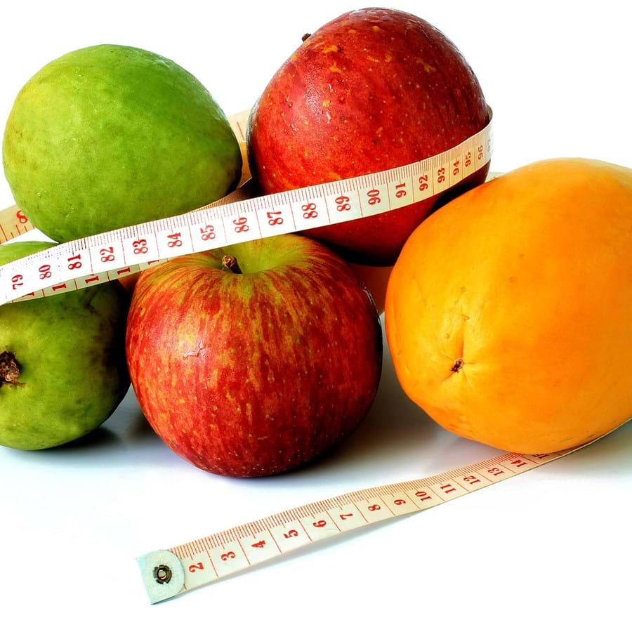 ein Maßband liegt zwischen zwei Birnen, Mangos und Äpfel