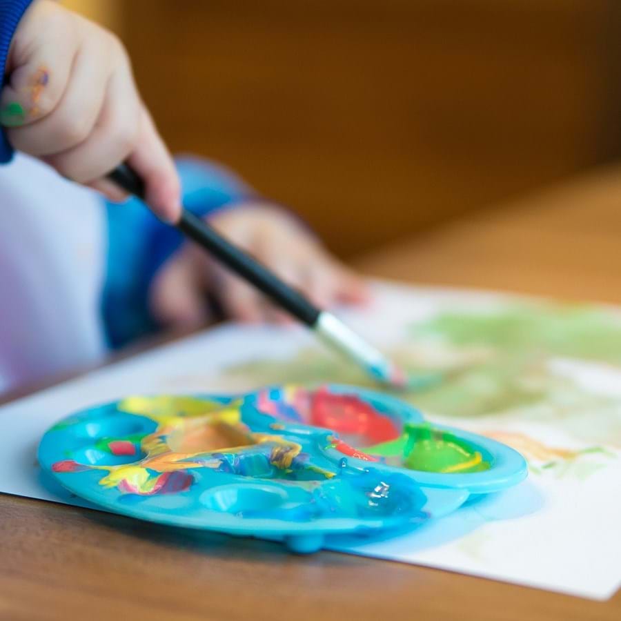 Ein Kind malt mit Wasserfarben auf ein Blatt Papier