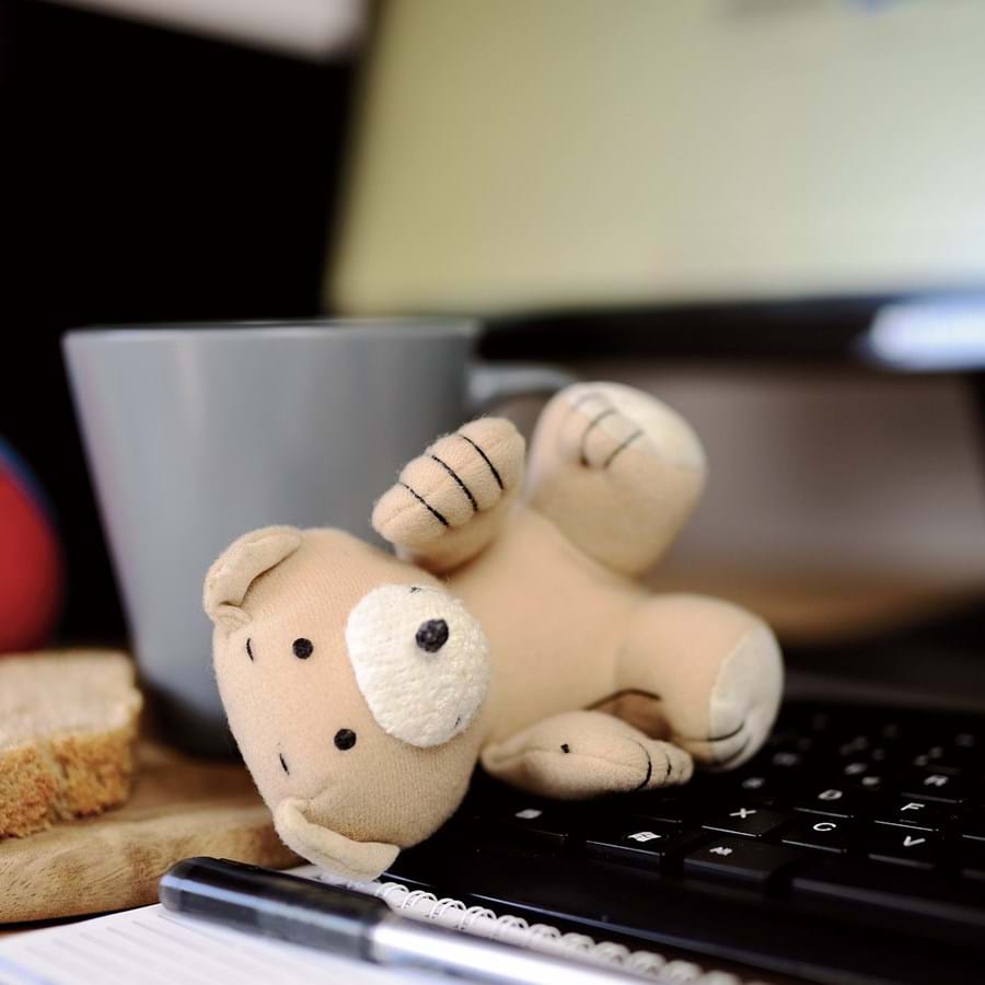 Arbeitsplatz mit Tastatur, Teddy, Kaffeetasse und einer Scheibe Brot