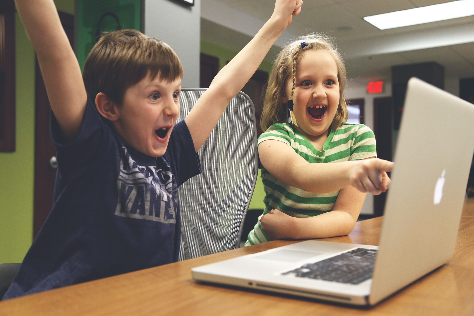 Zwei Kinder sitzen vor einem Laptop und freuen sich