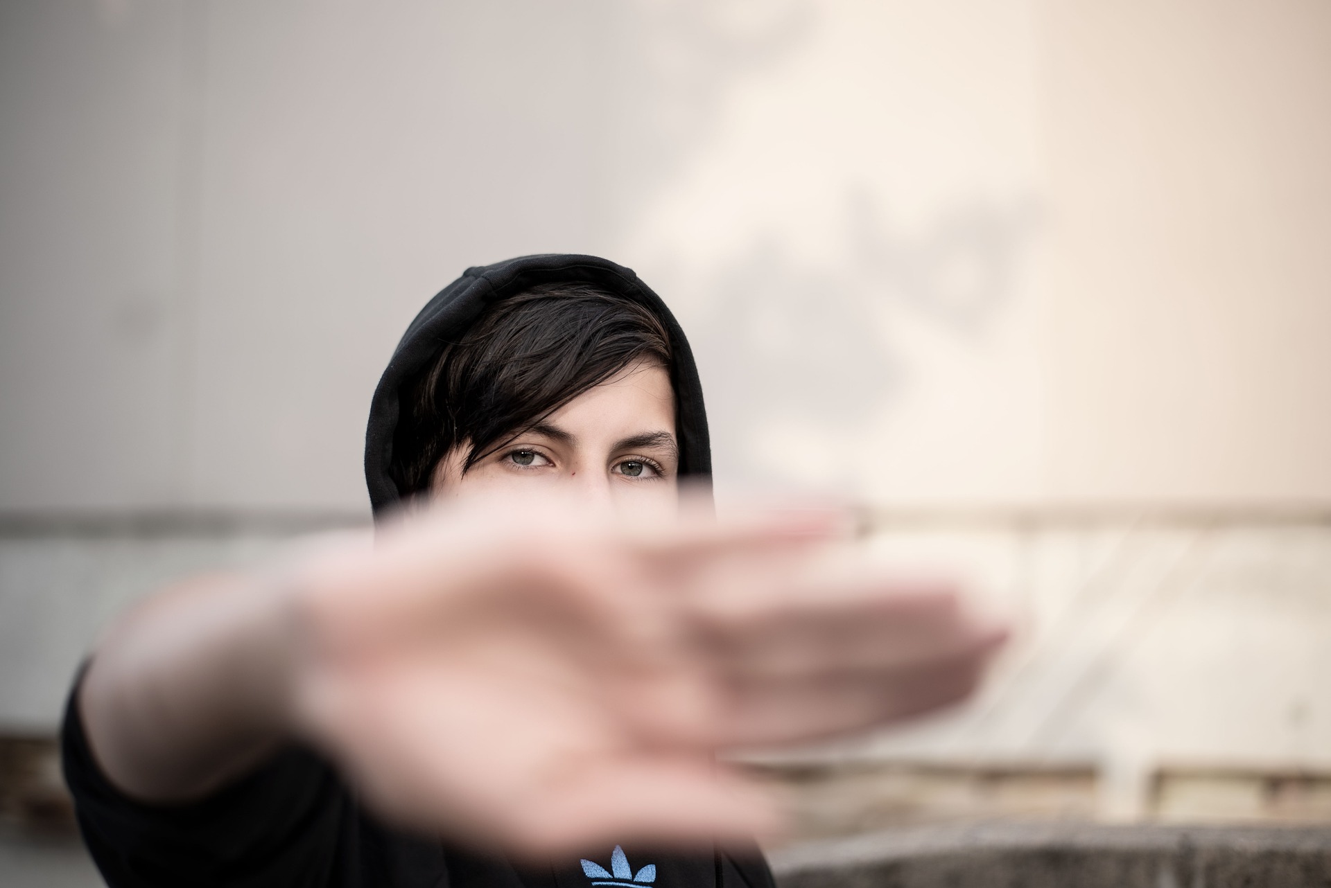 Teenager steht im Bild und schützt sich mit der Hand gegen die Kamera